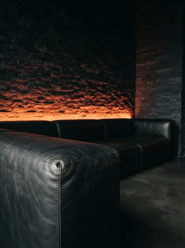 Vermilion light washing a stone wall beyond the armrest of a black leather sofa