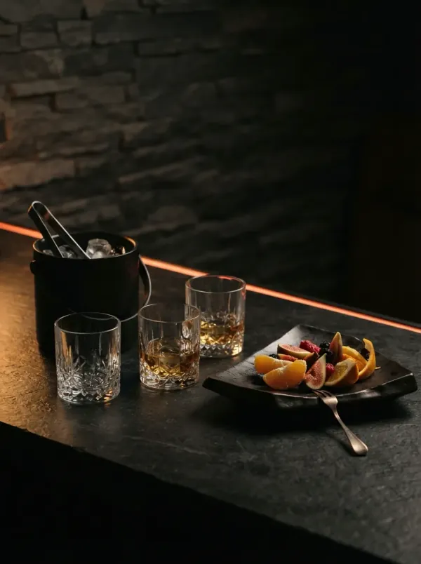 Three glasses, an ice bucket and a plate of fruit on a black stone tabletop